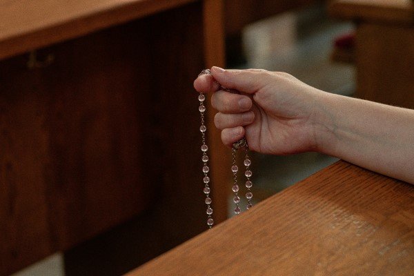 Como rezar el rosario: mano sosteniendo un rosario de cuentas claras, simbolizando esta devoción en la práctica católica.