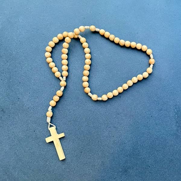 Santo Rosario de hoy: Rosario de cuentas de madera con cruz sobre fondo azul, representando la devoción y la oración diaria.